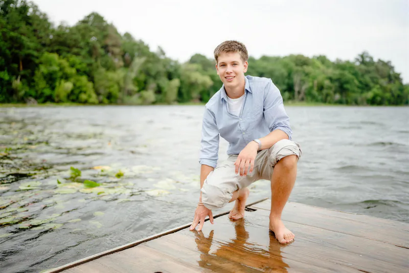 Jesse, crouched on a dock with one hand in the water, a wooded lakeshore behind him.